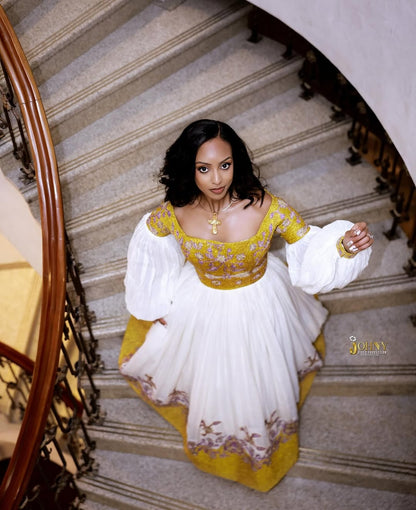 Woman in a yellow and white Gold Ethiopian Kemis standing on a staircase
