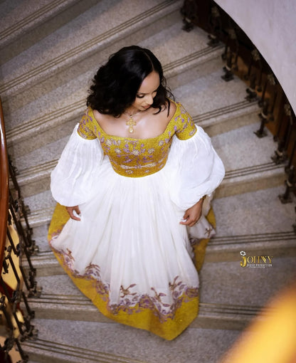Woman in a yellow and white Gold Ethiopian Kemis standing on a staircase
