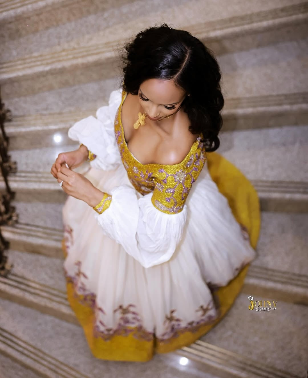 Woman in a traditional Gold Ethiopian Kemis with yellow and white colors sitting on steps.