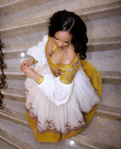 Woman in a traditional Gold Ethiopian Kemis with yellow and white colors sitting on steps.