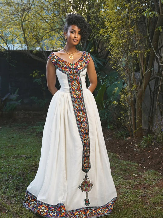 Woman wearing a white Habesha Dress with colorful embroidery standing outdoors.