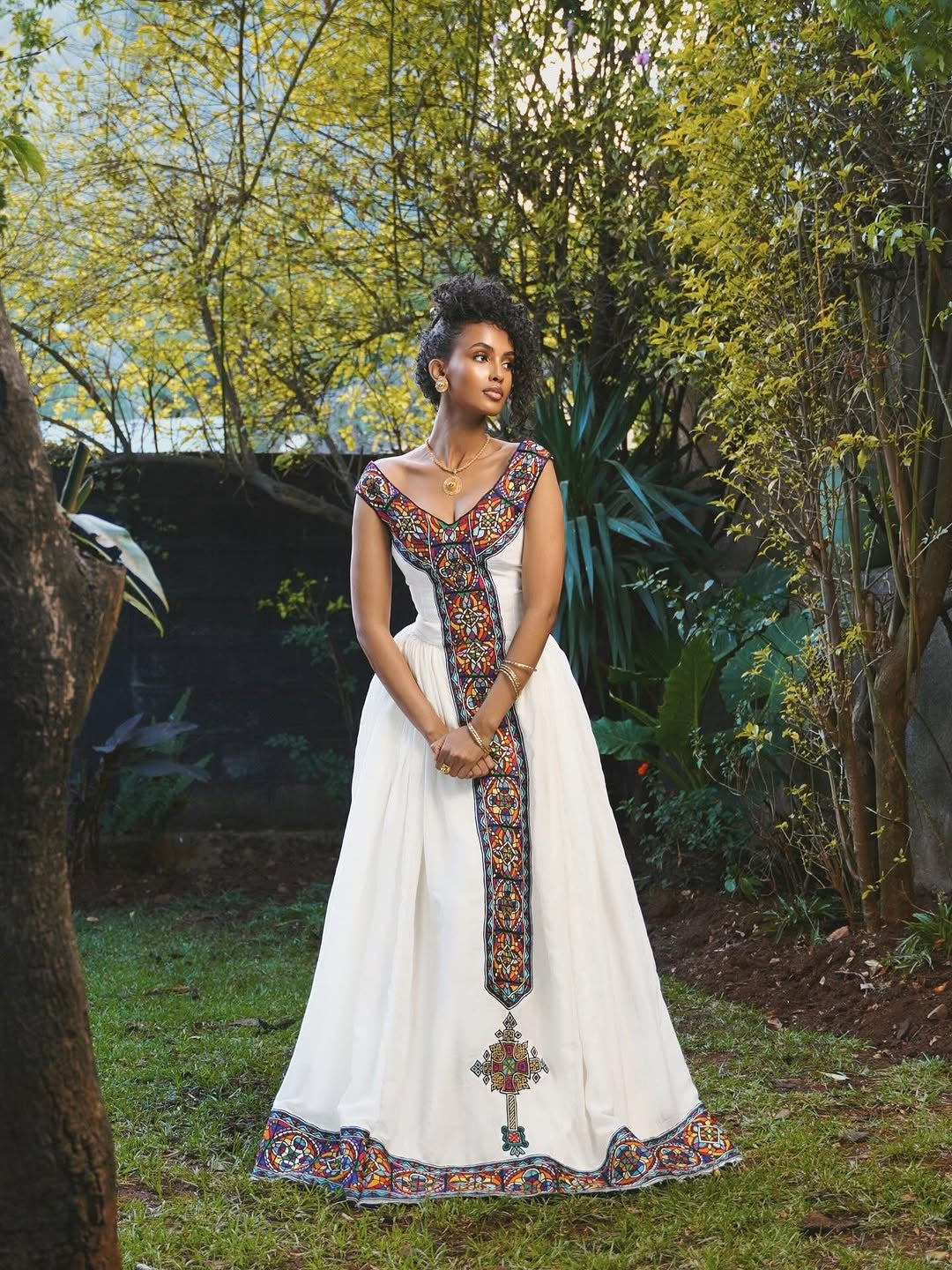 Woman in a long, ornate dress standing outdoors with trees in the background
