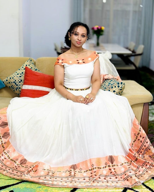 Woman in a white and orange traditional outfit sitting on a couch in a living room.