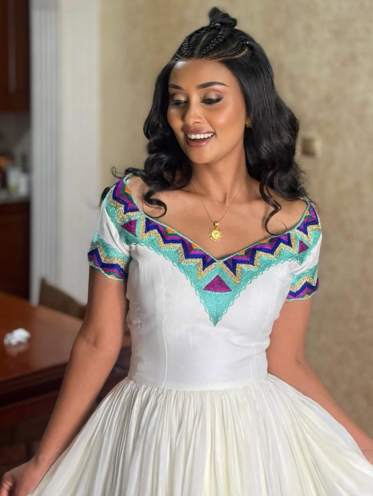 A woman wearing a white ball  Ethiopian Dress with a colorful geometric patterned bodice, featuring purple, teal, and gold accents, in an indoor setting.
