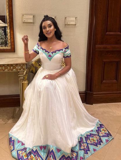 Woman in a white  Ethiopian Dress with colorful patterns in an indoor setting