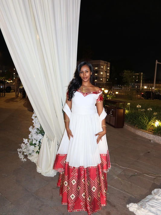 Woman in a white and red Habesha Kemis   standing next to a white curtain at night.