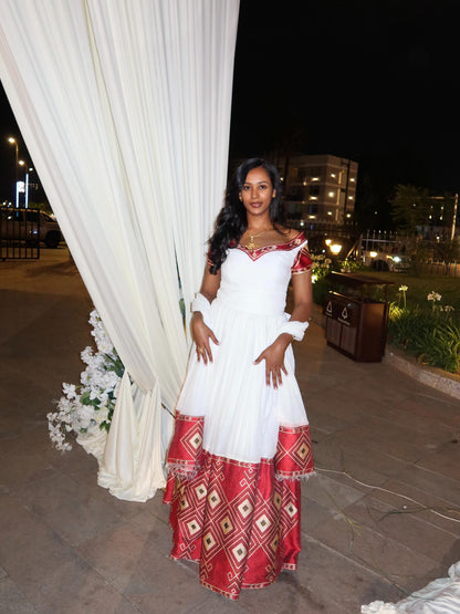 Woman in a white and red Habesha Kemis standing in front of a white curtain with flowers at night.