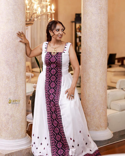 Woman in a white and purple Ethiopian Dress standing in an elegant interior setting.