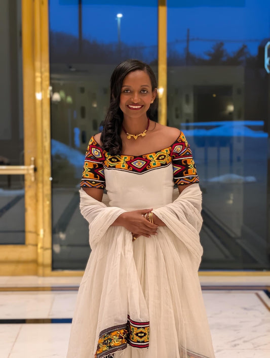 Woman in a traditional Ethiopian Traditional Dress standing in front of a glass door.