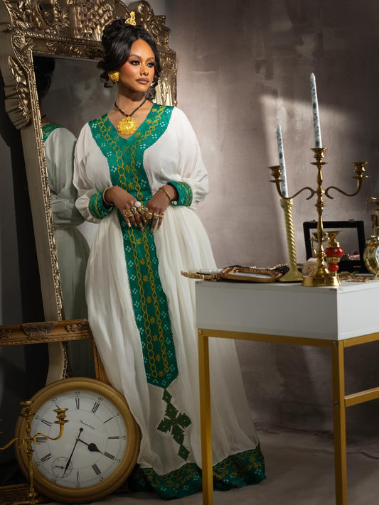 Woman in a white and green traditional Habesha Kemis standing in front of a mirror with decorative elements.