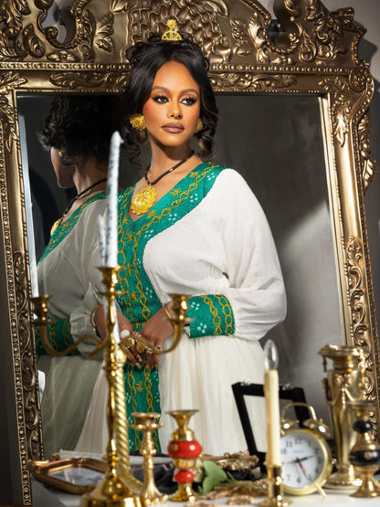Woman in traditional Habesha Kemis standing in front of an ornate mirror with candles and decorative items.