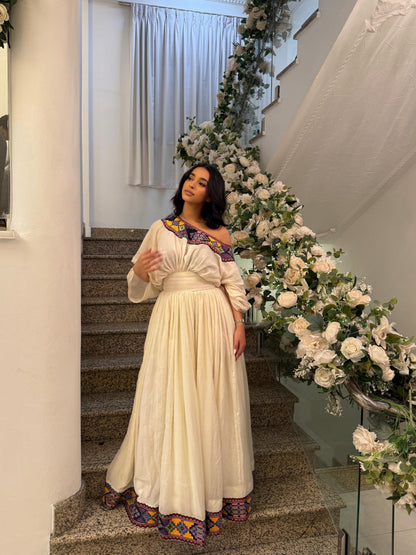 Woman in a long, elegant Habesha kemis standing on a staircase with floral decorations.