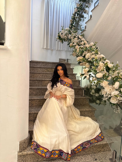 Woman in a white Habesha kemis with colorful embroidery sitting on a staircase.