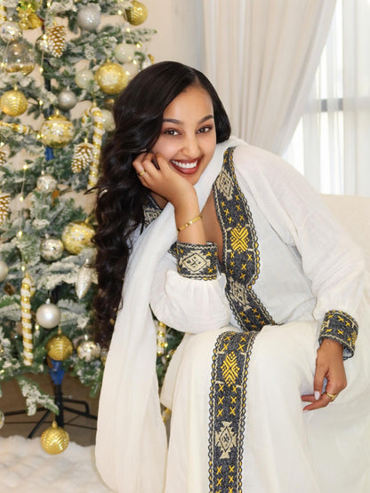 Woman in a white embroidered Ethiopian Traditional Dress sitting in front of a decorated Christmas tree.