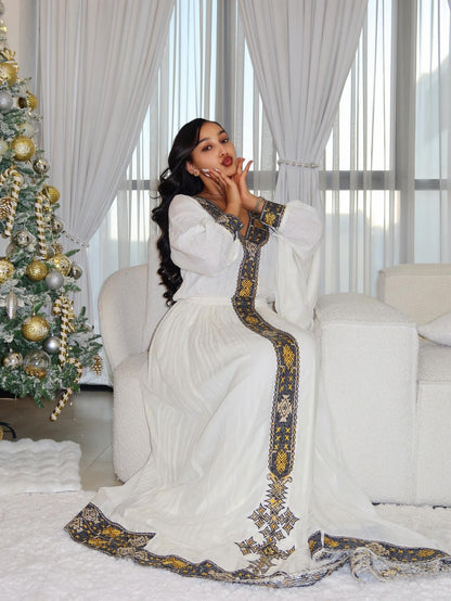 Woman in a white dress with gold Ethiopian Traditional Dress sitting in a decorated living room with a Christmas tree.