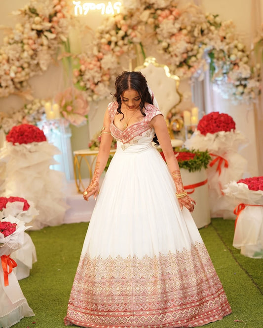 Woman in a white and pink traditional Pink Ethiopian Wedding Dress standing in front of floral decorations.