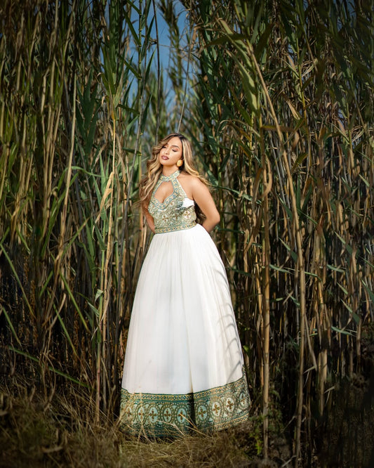 Woman in a white and green Ethiopian dress standing among tall plants