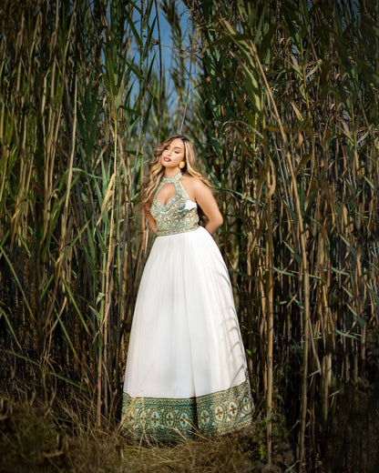 Woman in a white and green Ethiopian dress standing among tall plants