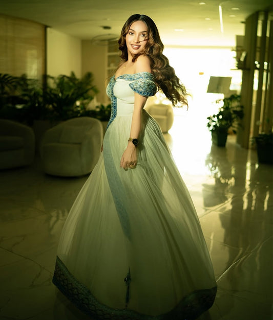 Woman in a white and blue habesha dress in an elegant interior setting.