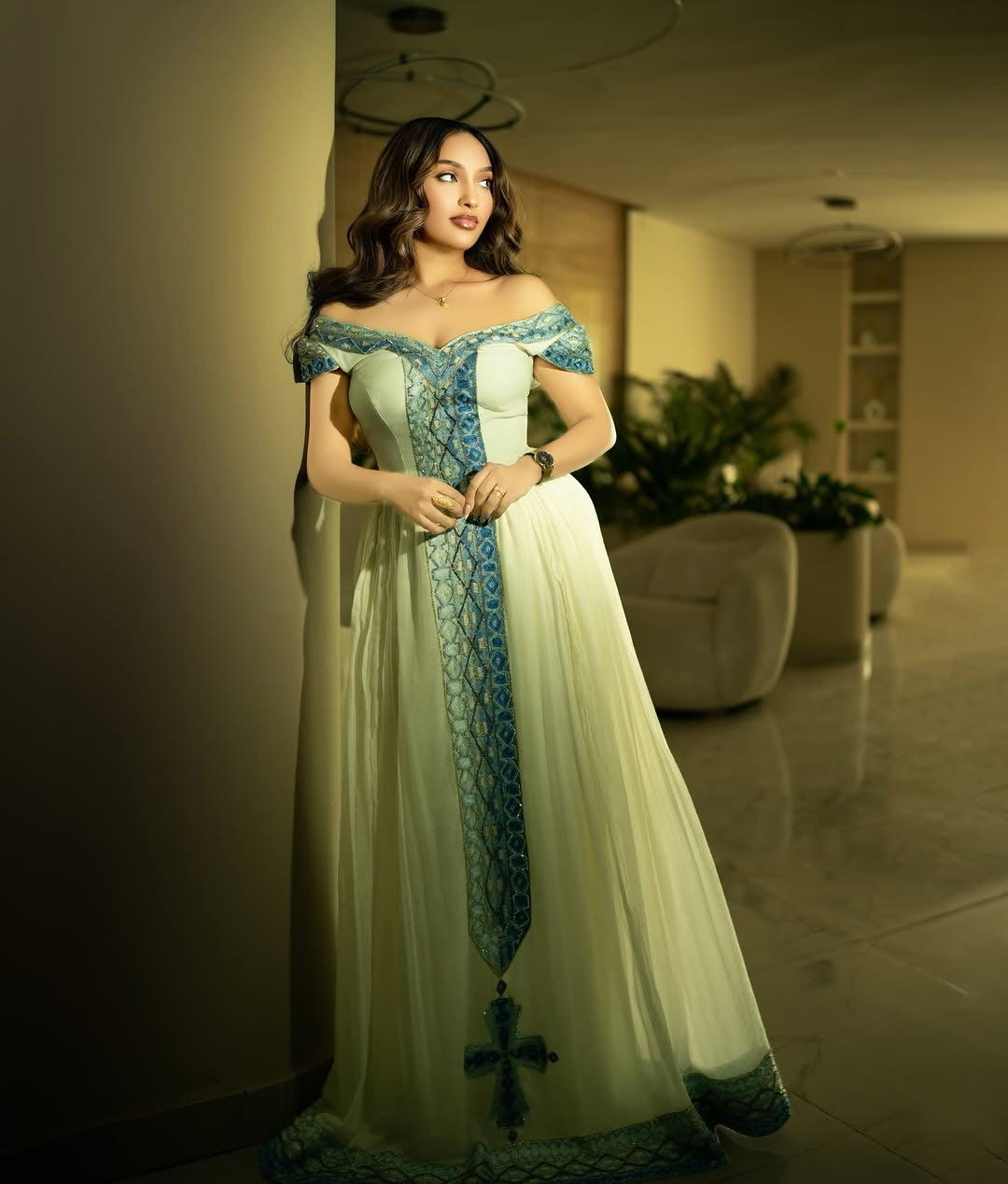 Woman in a white and blue Ethiopian dress standing in an indoor setting.