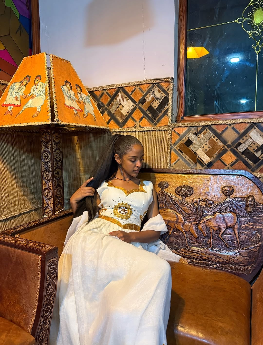 Woman in a white dress sitting in a decorated vehicle with intricate woodwork and a colorful lampshade.