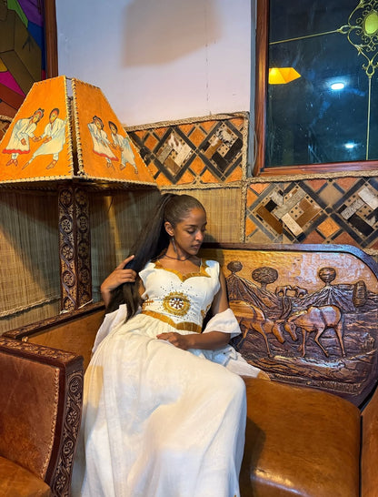 Woman in a white dress sitting in a decorated vehicle with intricate woodwork and a colorful lampshade.