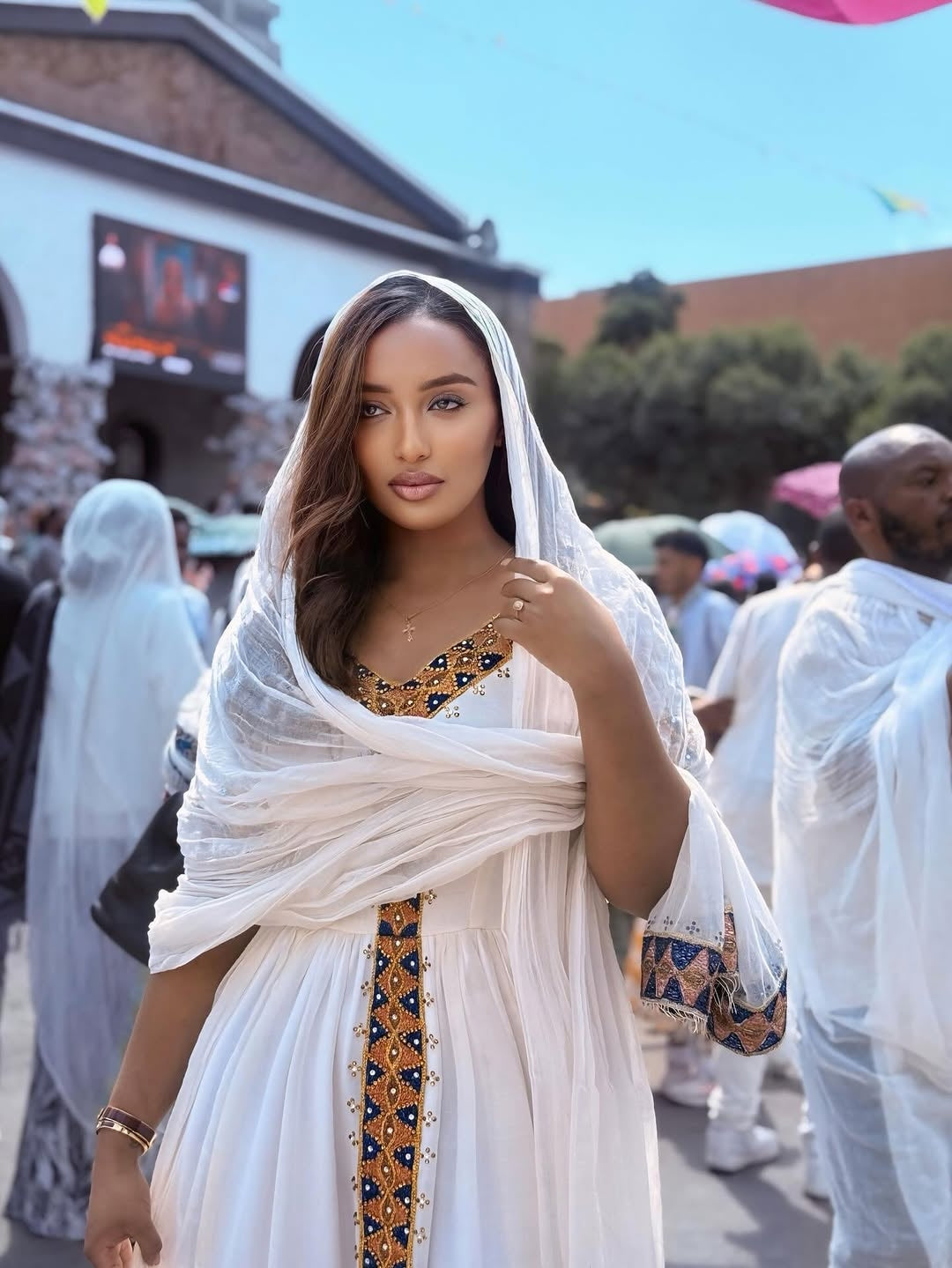 Woman in a white and gold Ethiopian Habesha Dress with a veil, standing outdoors.