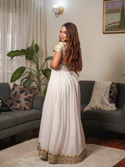 Woman in a white and gold Gold Habesha Libs standing in a living room.