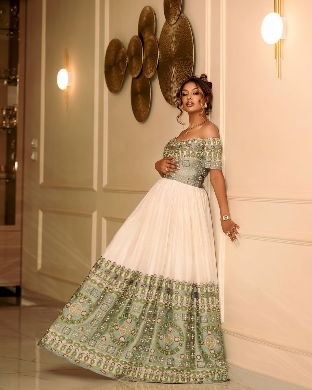 Woman in a traditional wedding dress with green and white patterns in an indoor setting.