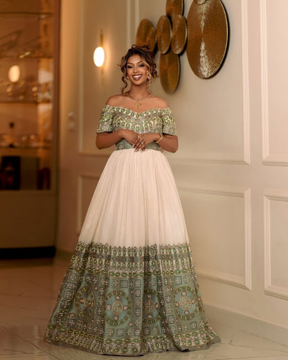 Woman wearing a traditional off-shoulder dress with green and white patterns in an elegant indoor setting.