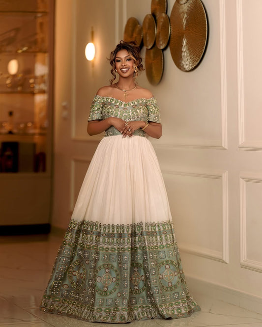 Woman wearing a traditional off-shoulder dress with green and white patterns in an elegant indoor setting.