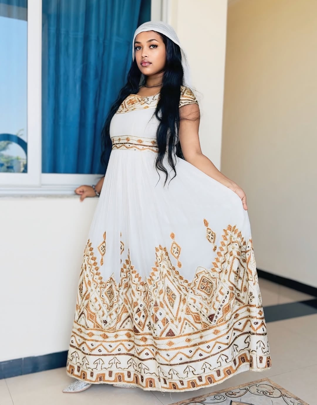 Woman wearing a white Ethiopian traditional dress with gold patterns indoors