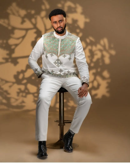 Man sitting on a chair wearing an embroidered Men’s Traditional Shirt and white pants against a brown background