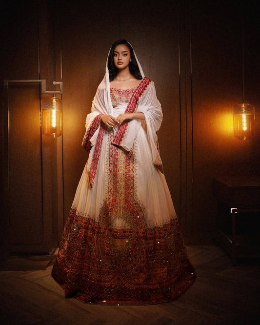 Woman wearing a traditional embroidered Ethiopian National Dresses in a dimly lit room with warm lighting.