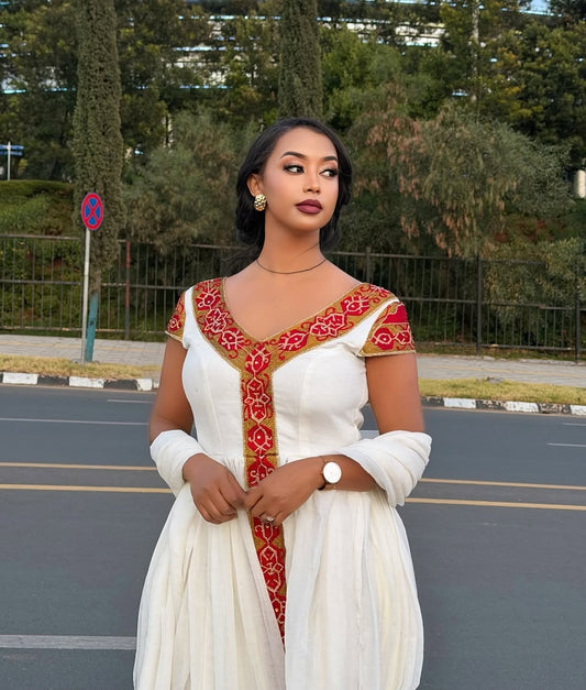 Woman in a white and red Ethiopian Dress outfit standing on a road with greenery in the background
