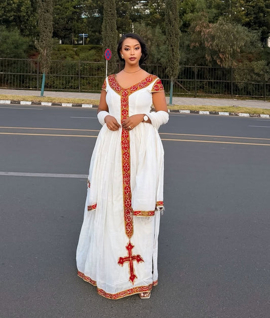 Woman in a white Ethiopian Dress with red embroidery standing on a road.